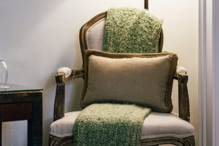 An ornate chair with a green blanket and a decorative pillow on it at The Charles Hotel in Niagara-on-the-Lake.