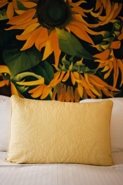 A decorative pillow on a bed in front of a sunflower art piece in Niagara-on-the-Lake.