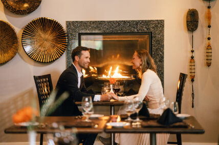 A couple eating in a dining room by a fireplace as part of the Niagara's finest romance package.